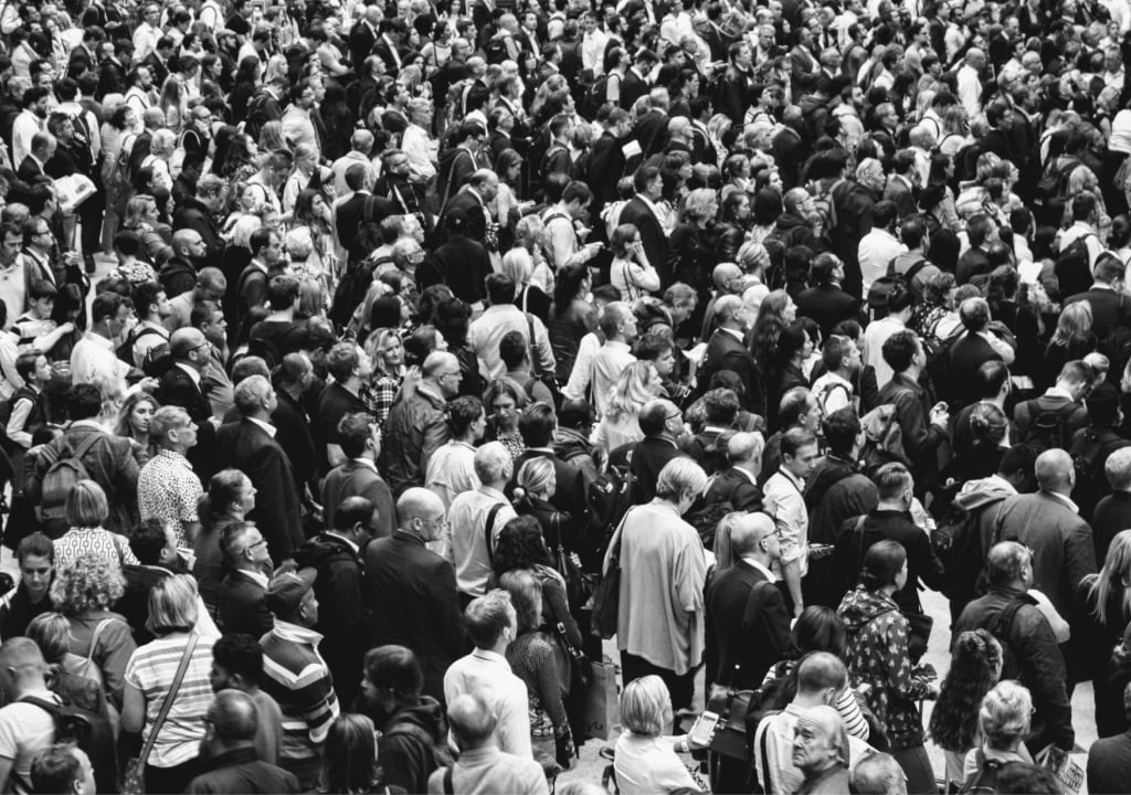 Black and white image of close up of large number of people gathering together in open space 