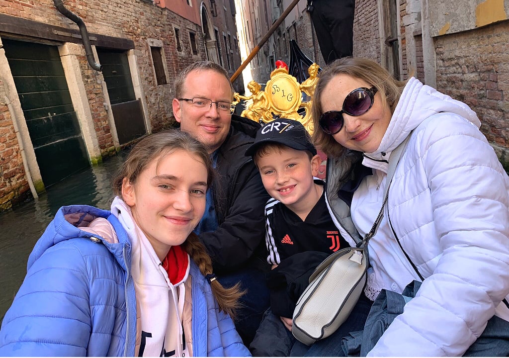 A man, a woman, a boy and a girl, all smiling, while sitting in a gondola in a canal 