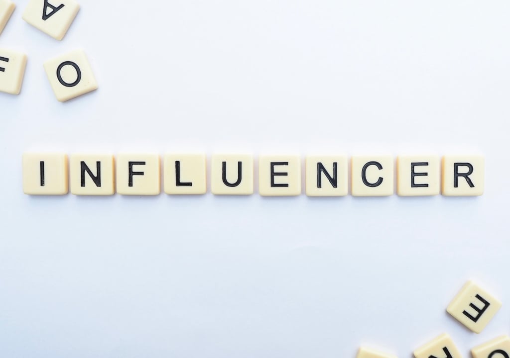 the word influencer made up of scrabble letters against white a board 