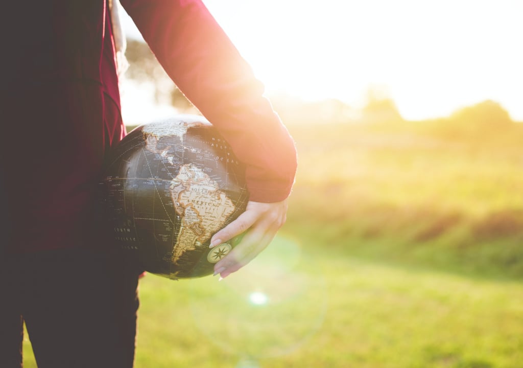 Person holding a small ball in the shape of the earth and looking towards the rising sun 